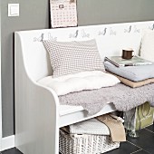 White, rustic bench with bird motifs, scatter cushions and lambskin rug against grey-painted wall