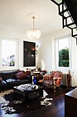 Crystal chandelier above classic leather sofa, cubic coffee table on cowhide rug and Baroque armchair