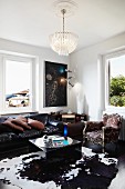 Crystal chandelier above classic leather sofa, cubic coffee table on cowhide rug and Baroque armchair