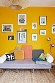 Various scatter cushions on simple couch below collection of pictures on yellow wall