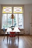 Retro chairs around kitchen table in front of window with stained glass upper panes in simple dining room