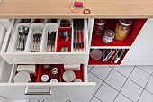 A view into open drawers in a kitchen unit with red and white cutlery and storage jar dividers