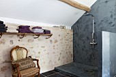 Antique armchair next to slate-grey, modern shower area in renovated country house with stone wall