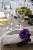 Blue anemone flower and floral napkin ring on linen napkin on charger plate next to rustic stemware