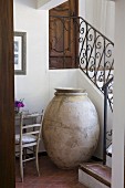 Old amphora for storing olives in niche below winding country-house staircase with wrought iron balustrade