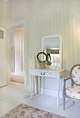 Small dressing table and antique chair with floral upholstery in white-panelled bedroom