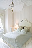 Bett mit Kopfteil in hellem, skandinavischem Schlafraum im eleganten Landhausstil