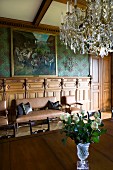Crystal chandelier above table with Biedermeier chairs in dining room of grand country house with leather sofa set below oil painting in background