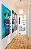 View along narrow hallway with rustic wooden floor and large modern artworks to gallery of pictures in living room