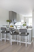 Bar stools with grey seats at counter in open-plan minimalist kitchen
