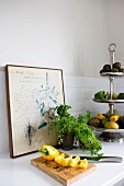 Sliced yellow pepper on wooden board, potted herbs, and fruits and vegetables on silver cake stand