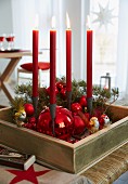 Adventskranz in Holzkasten mit roten Weihnachtskugeln und vier roten, brennenden Kerzen