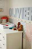 Soft toys on white chest of drawers in corner of nursery with ornamental letters on wall