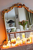 Brennende Stumpenkerzen in Weiß vor Spiegel mit antikem Goldrahmen, reflektierter Tulpenstrauss auf Couchtisch