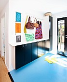 Foyer with pale blue lino floor, floating cupboards with black doors and bags hung from row of hooks on wall