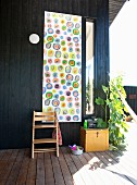 Tripp Trapp chair in front of wall hanging with pattern of colourful circles on black wooden terrace wall