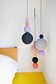 Strings of knitted balls hung next to bed above yellow wooden floor