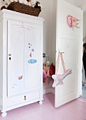 White, farmhouse wardrobe with nursery decorations next to fabric guitar hanging on open door
