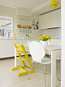 White retro shell chair and yellow-painted Tripp Trapp chair in white, modern, fitted kitchen with yellow accents