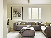 Modern grey sofa set with matching ottoman used as coffee table in traditional living room with black and white photo on wall