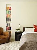 Brauner Ledersessel vor Bücherregal in Wandnische eingebaut und schwarzes, zylindrisches Nachtkästchen neben Bett
