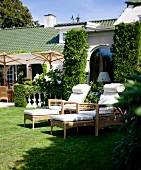 Pale wicker sun loungers with white cushions outside rustic house