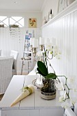 White orchid and candelabra holding white pillar candles on cabinet against white, wood-clad wall