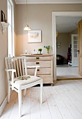 White-painted, rustic armchair on wooden floor in front of chest of drawers next to doorway