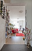 View into comfortable, open-plan living area with bookcase, retro standard lamp and flowering branches in doorway in renovated town-house apartment