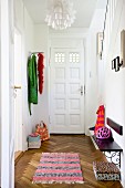 View through open door into hallway with rug, herringbone parquet floor, coat rack and wooden bench mounted on wall