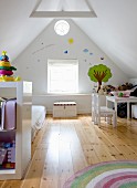 Child's bedroom in converted attic; shelving in front of futon on wooden floor, child's table and chairs against gable-end wall