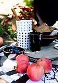 Red apples, bowl of blueberries and crockery on table outdoors