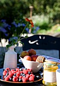 Bowls of fresh berries and plums and flower in ceramic vase on table outdoors