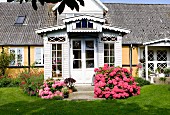 View from garden of pink hydrangeas flanking white-painted wooden porch of house