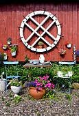 Old mill wheel and potted plants on Falu-red wooden wall behind garden furniture and flowers