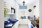 Narrow kitchen with accents of colour provided by blue accessories and striped Roman blind