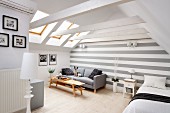 Heller Wohnraum mit sichtbarer Dachkonstruktion und grau-weiss gestreifter Rückwand, graues Sofa mit hellem Holztisch