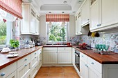 Modern, U-shaped fitted kitchen in country-house style with mixture of tiles on splashback, wooden worksurfaces and red and white striped roller blinds