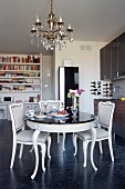 Eclectic dining area with chandelier in front of modern kitchen counter and bookcase in background