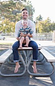 Father holding baby son sitting on outdoor table