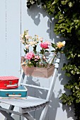 Bottles of flowers in window box and small, colourful, retro suitcases on garden chair against white wooden wall