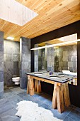 Designerbad mit Waschtisch auf rustikalem Holzbock und grauen Fliesen, Oberlichtschacht in der Holzdecke