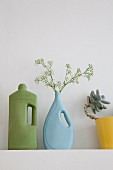 Industrial plastic bottles painted blue and green on shelf, one holding sprig of flowers