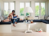 Mother and children on window seat with black seat cushion in renovated, white, country-house interior