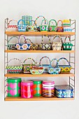Collection of colourful beaded baskets and printed tins on wall-mounted String shelves