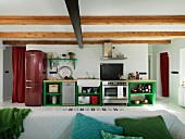Open-plan kitchen in rustic interior; counter with green-painted base units, dark red fridge-freezer