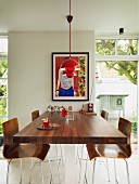 High, walnut table abutting wall and bar stools with wooden shell seats below red pendant lamps and between French windows