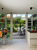Open-plan kitchen with dining area next to glass wall, open terrace doors and view of outdoor seating area