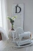 Old rocking horse next to vase of amaryllis on white-painted stool in front of decorative letter hung on removed door