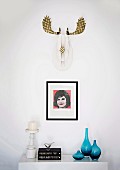 Stilisiertes, goldbemaltes Hirschgeweih und kleines Popart-Bild über skandinavischem Kerzenständer und eleganten, blauen Glasvasen